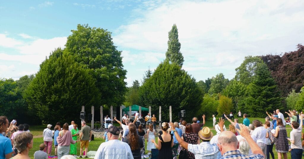 Crowd of people gathered in a park around tall white poles under a sunny sky