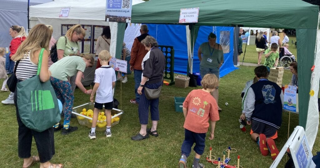 People and children at an outdoor event tent, looking at displays and playing on a small activity area
