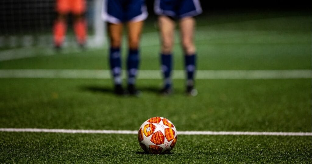 Football resting on the pitch with blurred players in the background