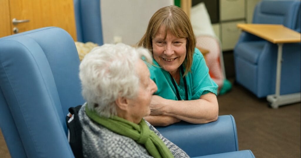 Woman smiling and talking with an elderly woman in a care home lounge