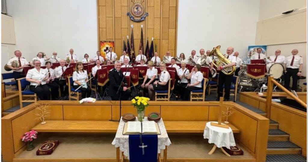 A church band seated on a raised stage in a sanctuary with a cross on the front table and a pulpit in the centre