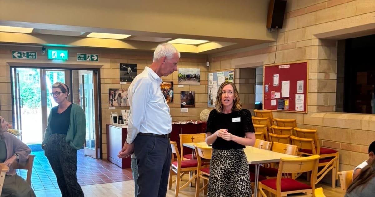 People conversing in a church hall with tables, chairs and fire exit signs