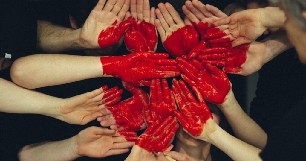 Multiple hands with red paint forming a circle against a dark background