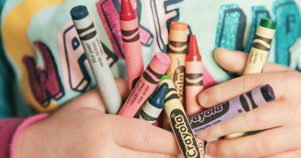 Hands holding assorted colorful crayons labeled Crayola