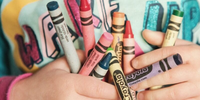 Hands holding assorted colorful crayons labeled Crayola