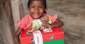 Smiling child holding a doll on a red and green cardboard box