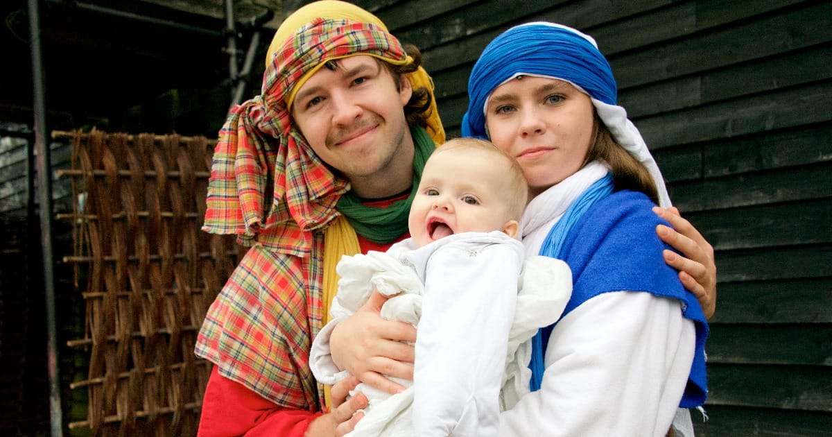Two adults holding a smiling baby, dressed in colorful historical-style clothing
