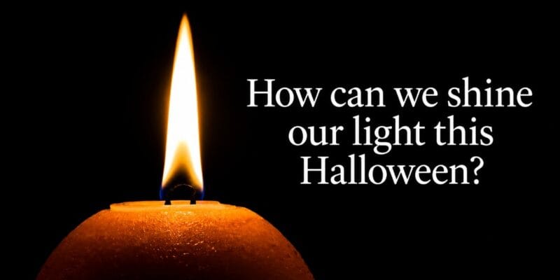 Lit orange candle beside text reading “How can we shine our light this Halloween?”