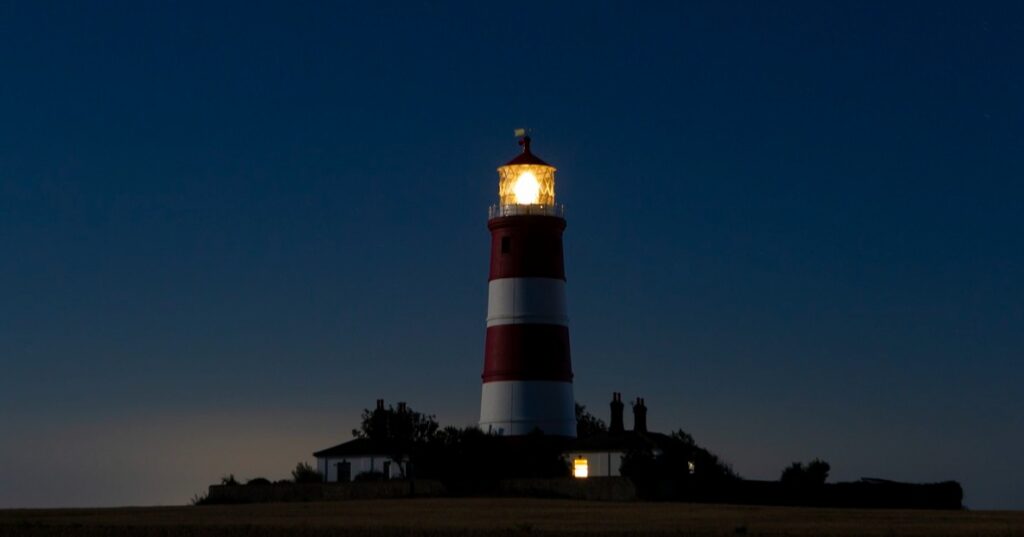 Red-and-white striped lighthouse with its lamp illuminated at dusk